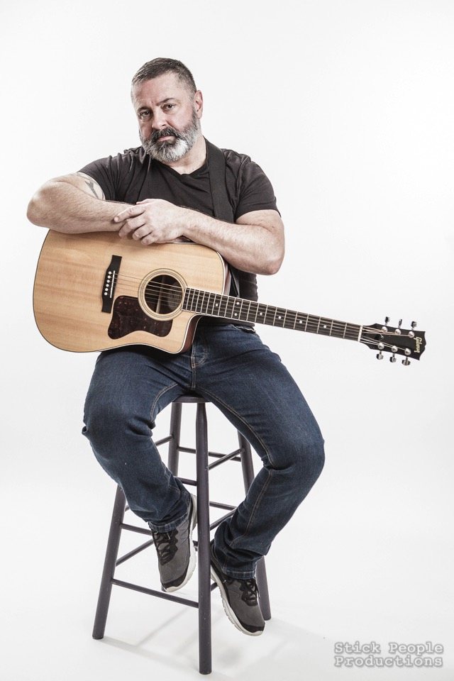 Coleman Jolley seated on a stool with an acoustic guitar