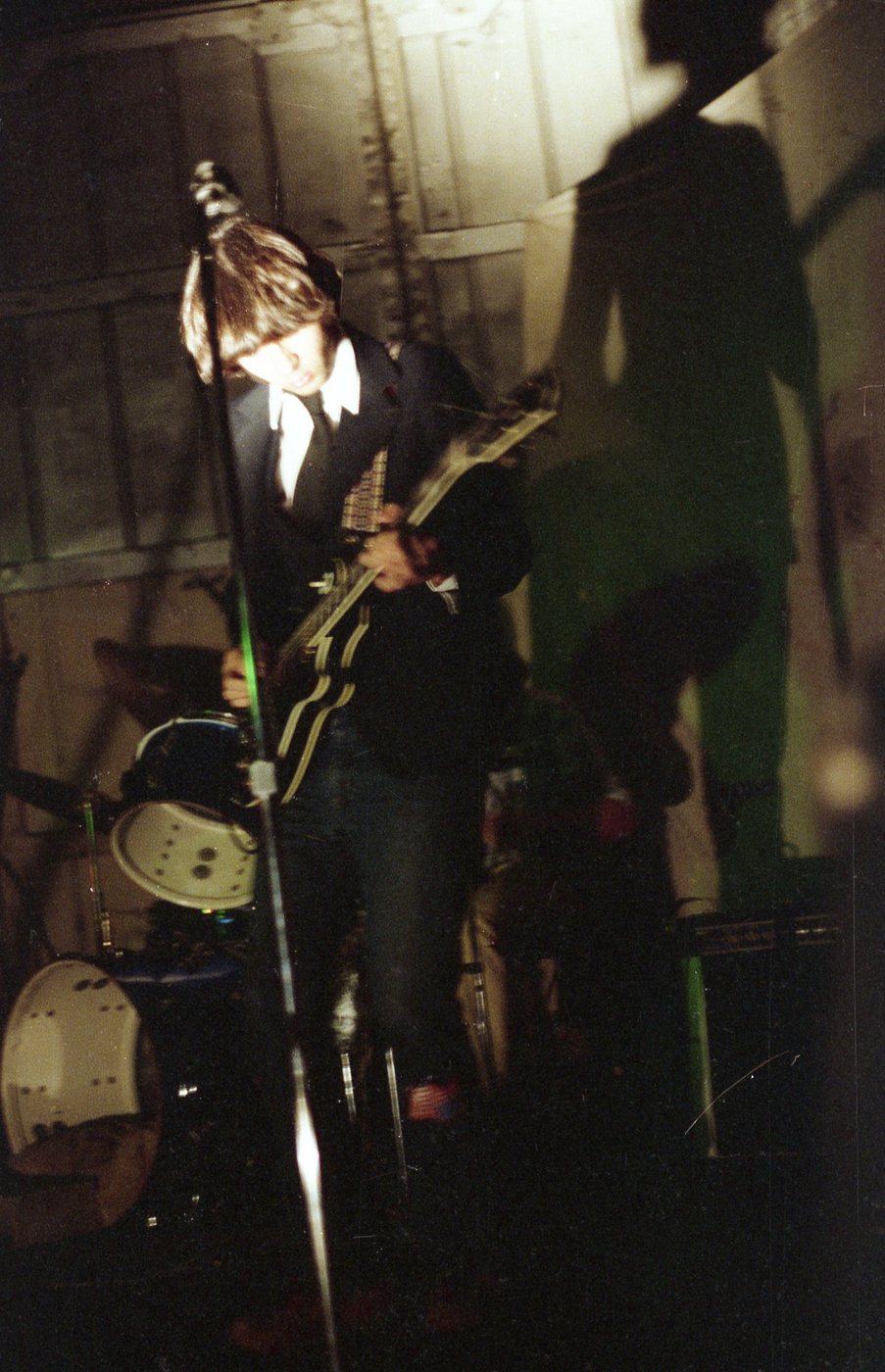 Young Coleman playing guitar at a microphone, a large shadow on the wall behind him